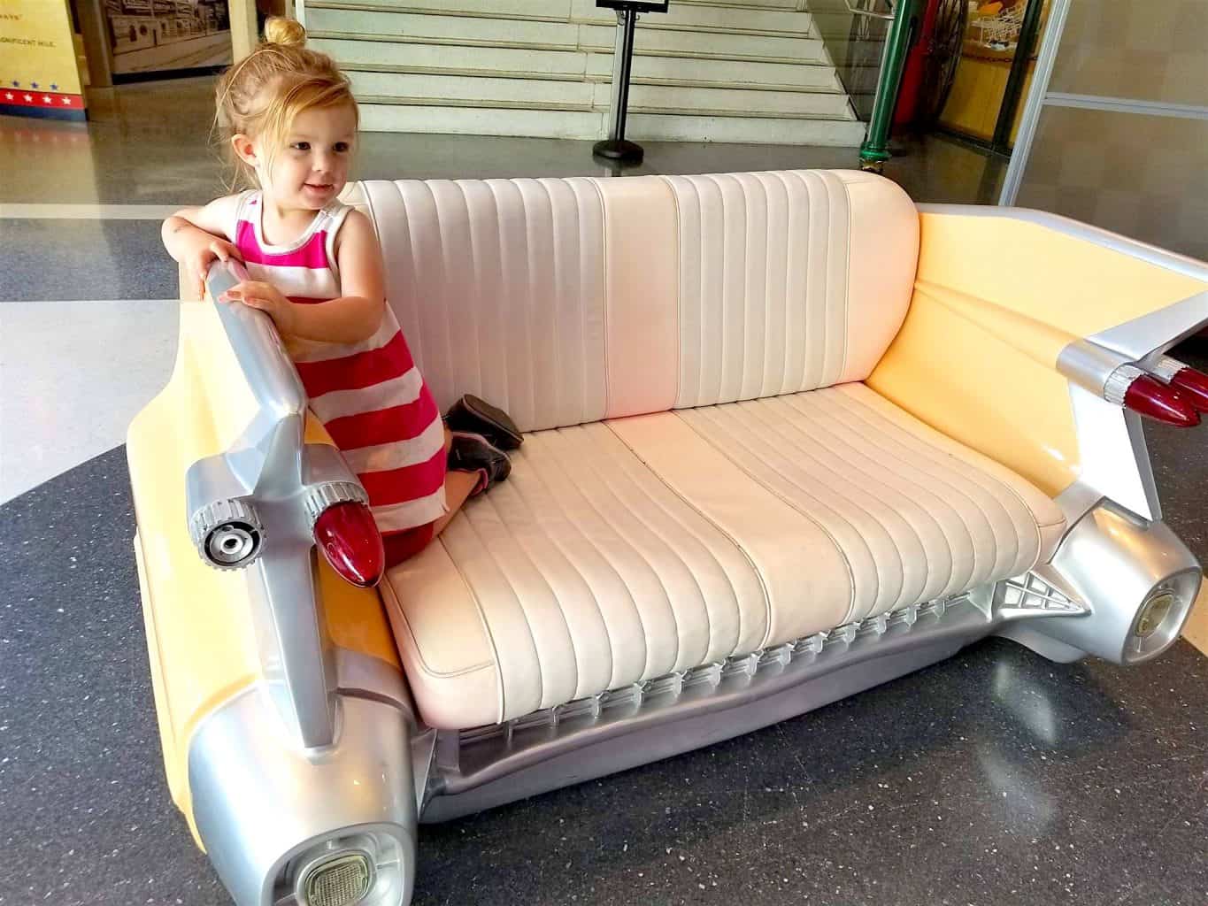 little girl on vintage car couch at a museum